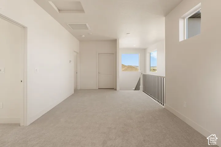Open landing area featuring neutral carpeting, high ceilings, multiple windows, and a metal spindle railing