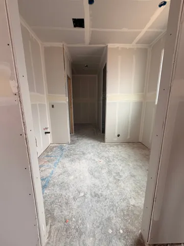 Unfinished interior hallway featuring drywall installation, electrical wiring, and a concrete subfloor
