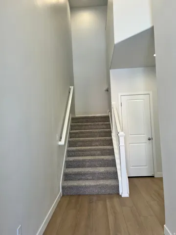 Carpeted staircase featuring white handrails and newel post, with recessed lighting overhead