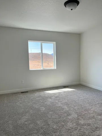 Spacious room featuring new gray carpet, white baseboards, and light gray painted walls