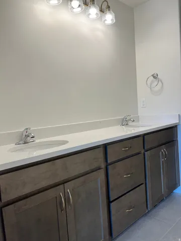Dual vanity featuring dark wood-finish cabinetry, light countertops, integrated sinks, and brushed nickel hardware