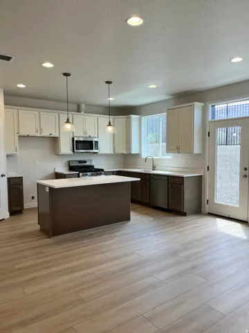 Open-concept kitchen featuring an island with a light-colored countertop, wood-finish flooring, two-tone cabinetry, stainless steel appliances, and recessed lighting