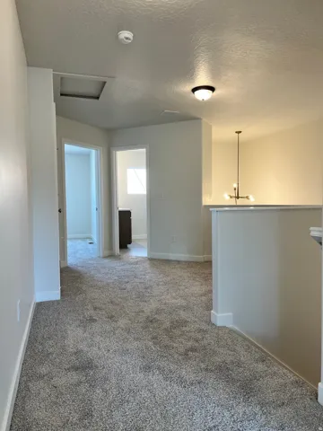 Carpeted interior hallway with multiple doorways and a contemporary chandelier