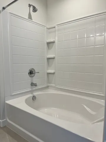 White bathtub and shower combination featuring a tiled surround, chrome fixtures, and integrated shelving