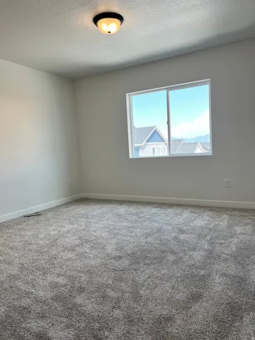 Spacious room featuring gray textured carpeting, white baseboards, and light neutral wall paint