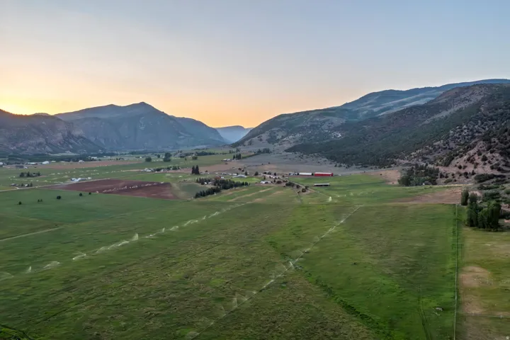 Expansive valley landscape featuring cultivated fields, distant mountain ranges, and scattered agricultural structures