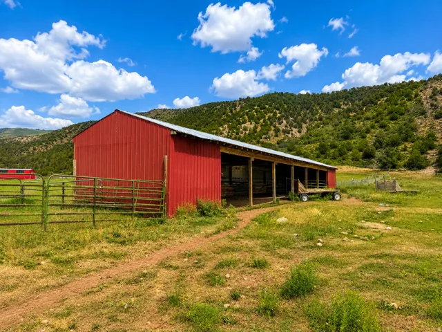 Red metal-sided barn with a silver-toned roof, featuring an open-sided lean-to structure supported by wooden posts