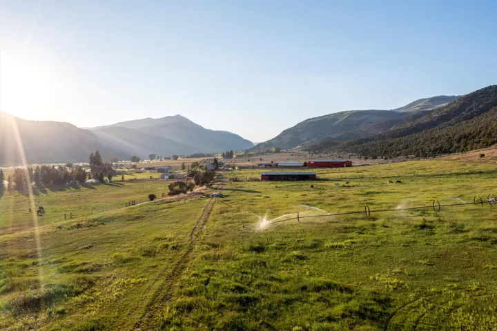 Expansive green pasture with irrigation sprinklers, surrounded by rolling hills and distant mountains