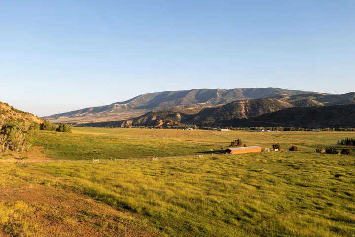Expansive green fields with a distant red-roofed barn, framed by rolling hills and a mountainous horizon under a clear sky