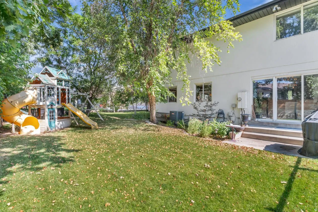 Expansive green lawn with mature trees and a multi-level play structure