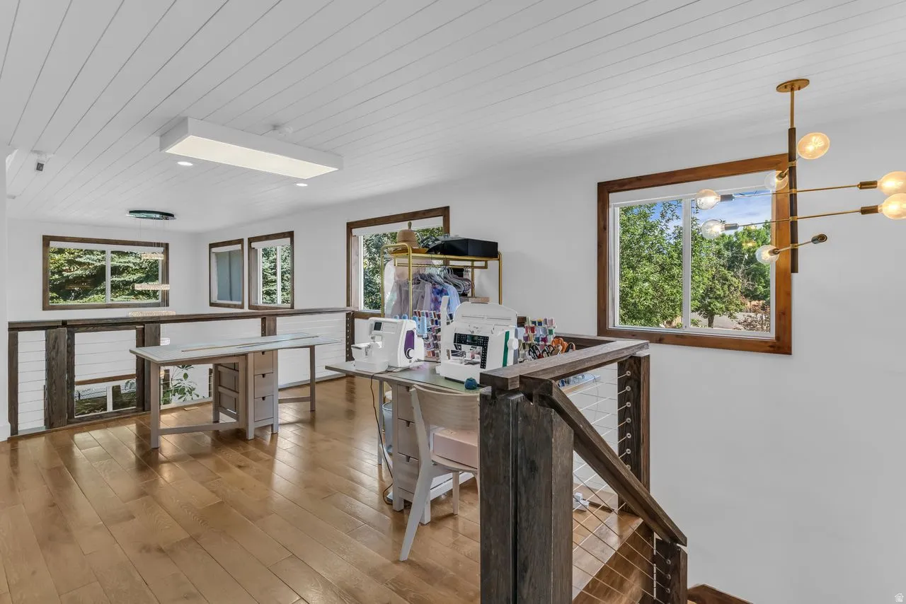 Spacious loft featuring hardwood flooring, white shiplap ceiling, multiple windows with dark wood frames, and a contemporary light fixture