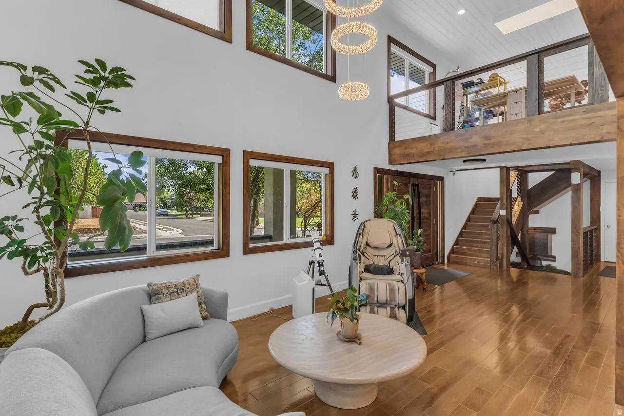 Two-story living area featuring a high vaulted ceiling, large chandelier, large windows with smart blinds, and hardwood floors.