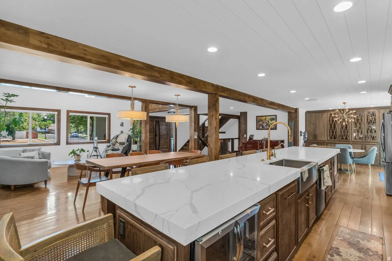 Expansive kitchen island a featuring light quartz countertop, integrated sink with a gold-tone faucet, and under-counter beverage refrigerator.