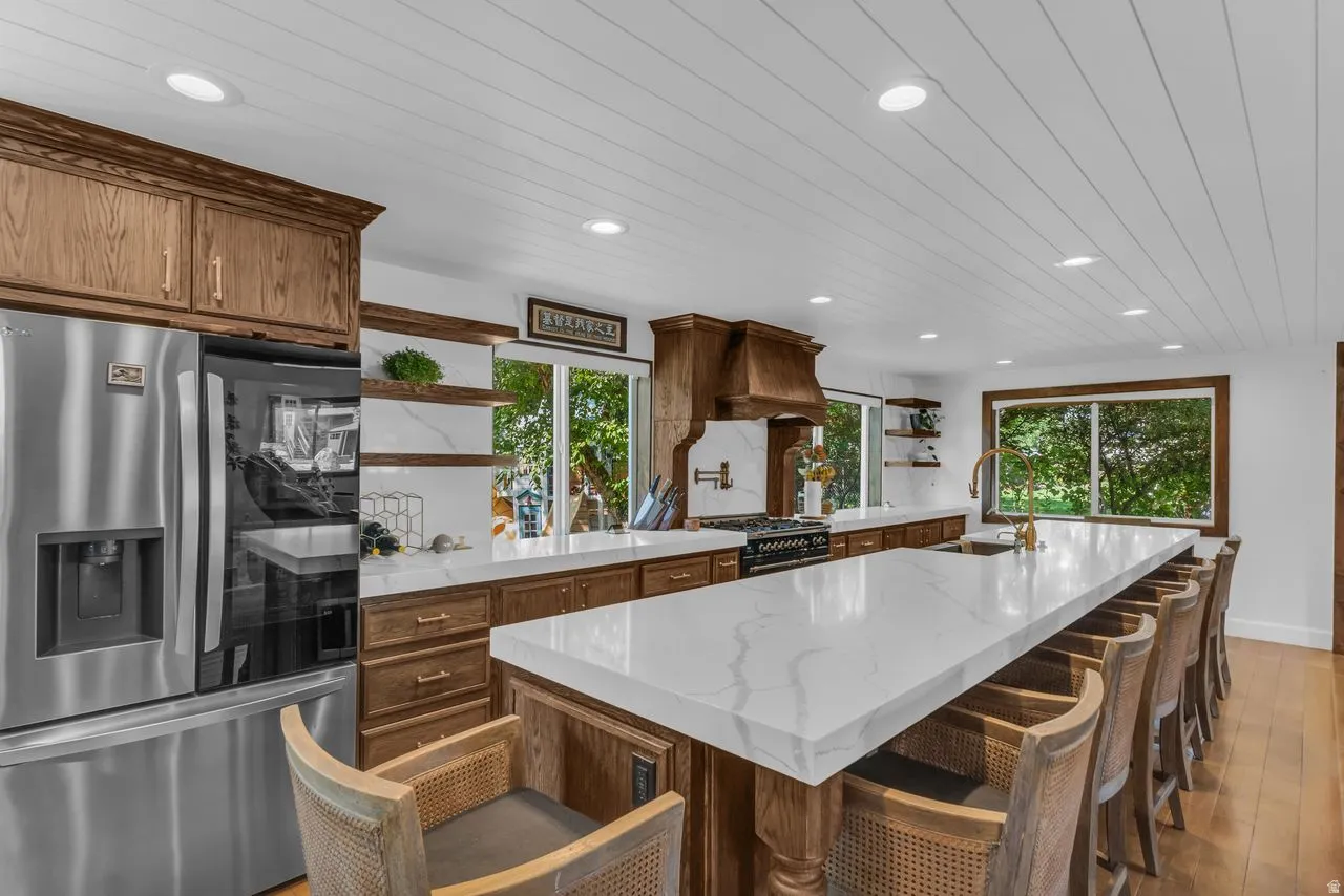 Gourmet kitchen featuring a large island with included seating, a professional-grade range with a custom wood hood, stainless steel refrigerator, white quartz countertops, and custom wire-brushed oak cabinetry