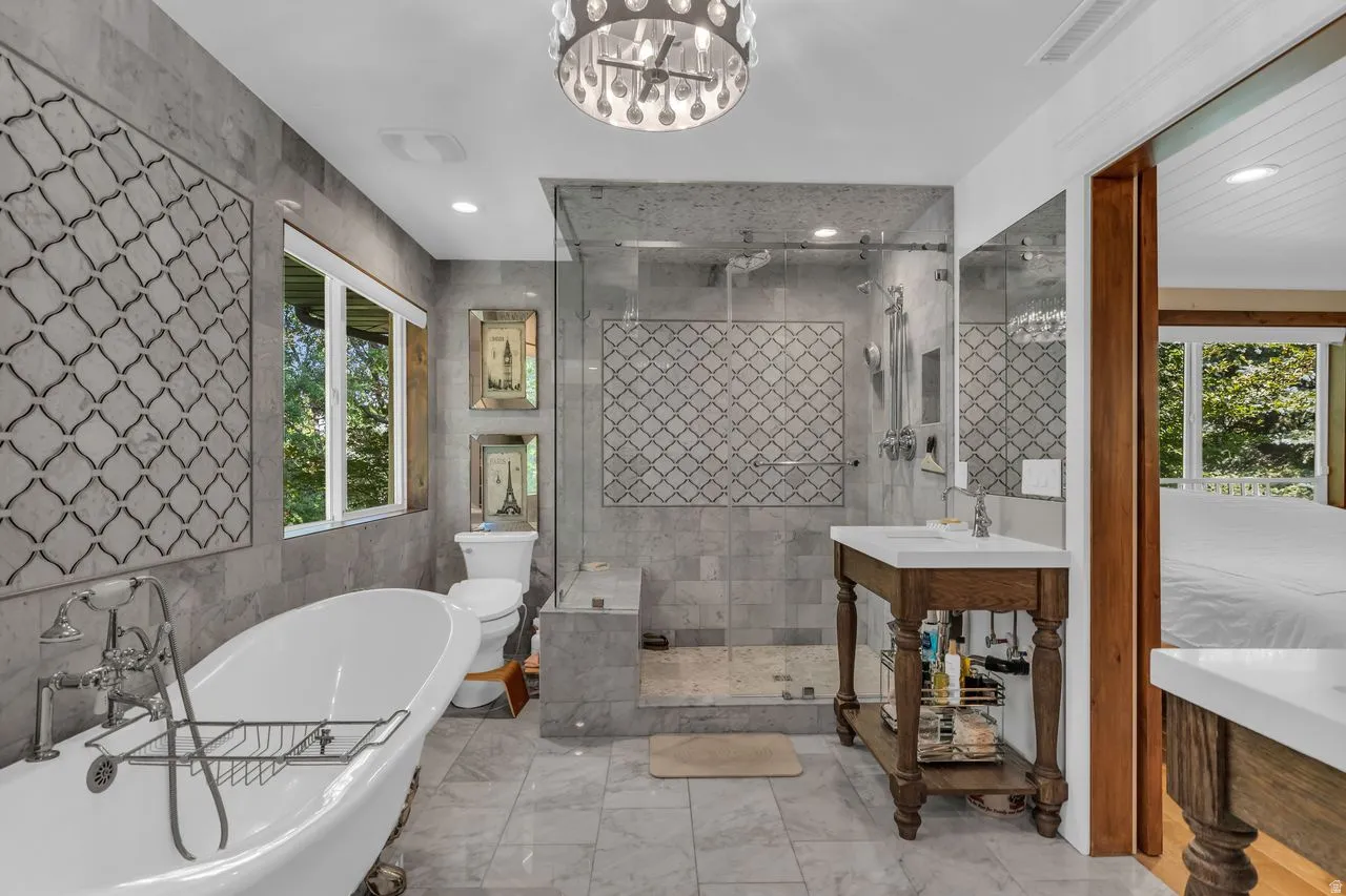 Ensuite bathroom featuring a freestanding clawfoot tub, a walk-in glass-enclosed shower, and decorative accent tiling