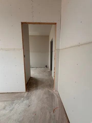 Unfinished interior hallway featuring drywall installation, unfinished door frames, and exposed subfloor