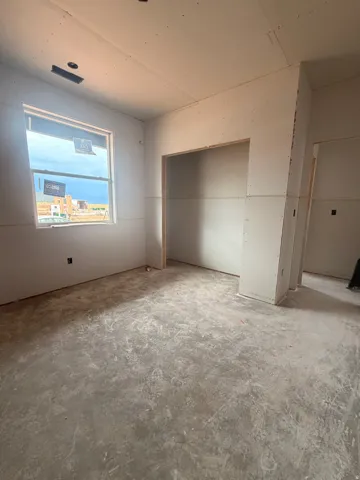 Room under construction featuring drywall installation, unfinished flooring, a single window, and an open doorway
