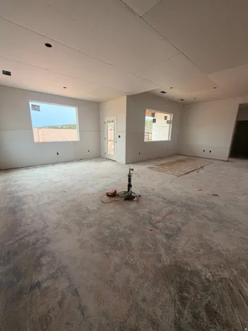 Spacious open-concept interior featuring a concrete subfloor, multiple windows providing natural light, and a white paneled door