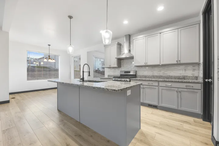 Kitchen featuring a central island with a sink, granite countertops, light gray cabinetry, stainless steel appliances, and wood-finish flooring