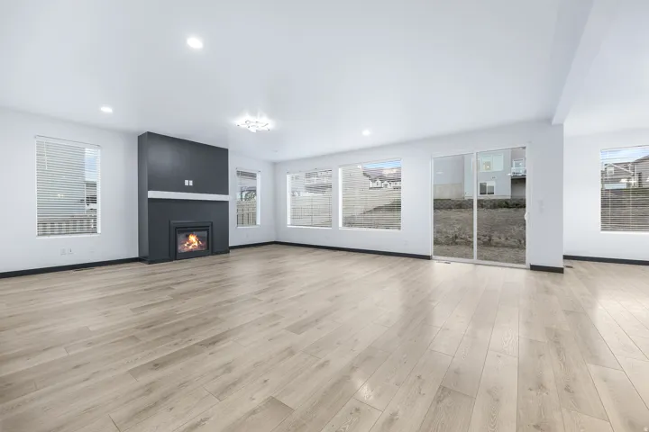 Spacious room with wood-finish flooring, a contemporary fireplace with a dark surround, recessed lighting, and a sliding glass door to the exterior