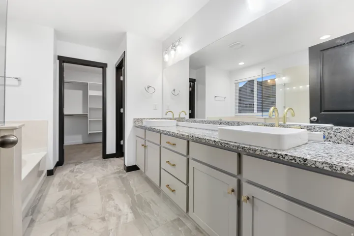 Double vanity featuring granite countertops, undermount cabinetry, and gold-finish faucets
