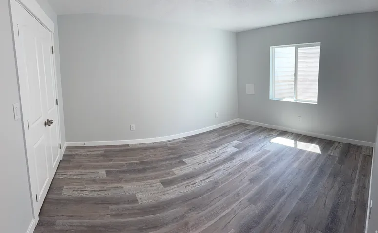 Spacious room featuring wood-finish flooring, light grey walls, white baseboards, and a white paneled door