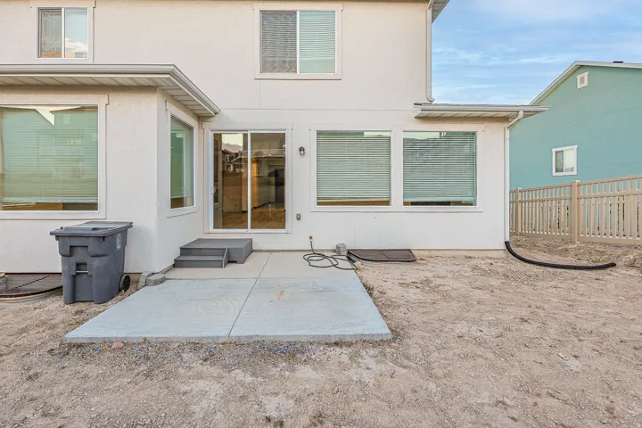 Rear exterior featuring a concrete patio, sliding glass door entry, and multiple windows with blinds