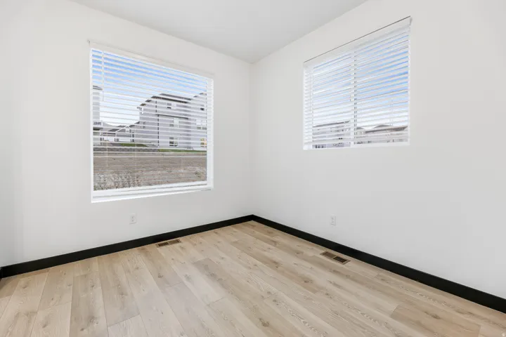 Light-filled room featuring two windows with horizontal blinds, light-toned wood-finish flooring, white walls, and dark baseboards