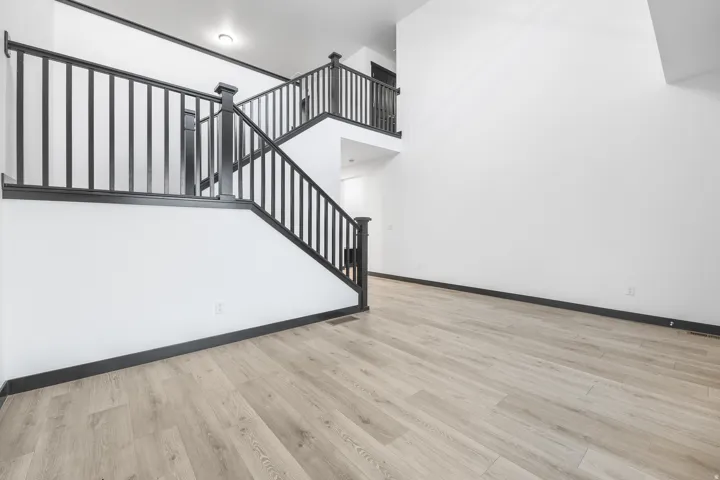 Two-story entry featuring light wood-finish flooring, a contemporary staircase with black railings, high white walls, and dark baseboards