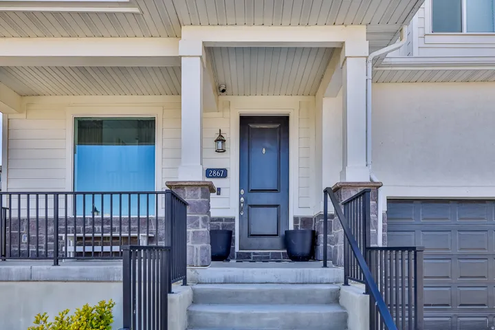 Inviting front entrance featuring a dark paneled door, stone accents, and a porch with black metal railings
