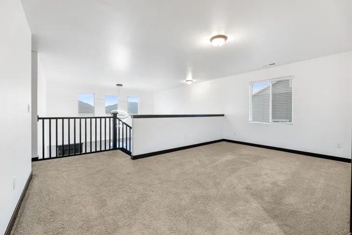 Open loft area featuring neutral-toned carpeting, white walls, and black baseboards