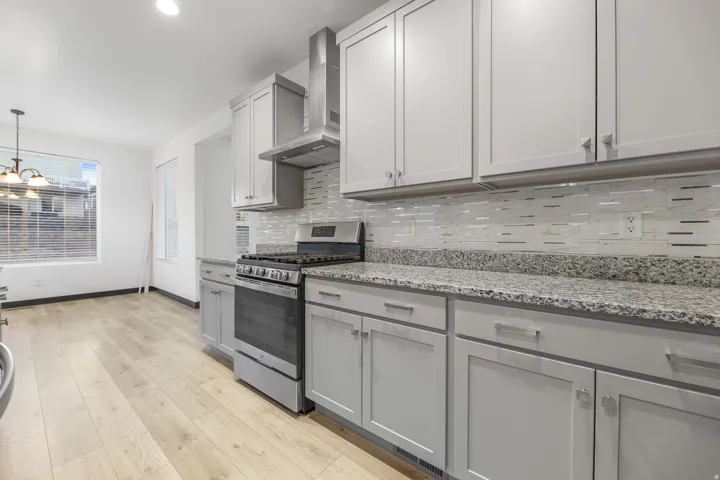 Modern kitchen featuring light gray cabinetry, stainless steel appliances, granite countertops, a tiled backsplash, and wood-finish flooring