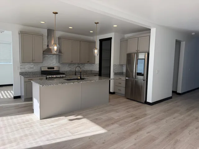 Kitchen featuring wood-finish flooring, an island with countertop, a stainless steel gas range with a matching hood, and a stainless steel refrigerator