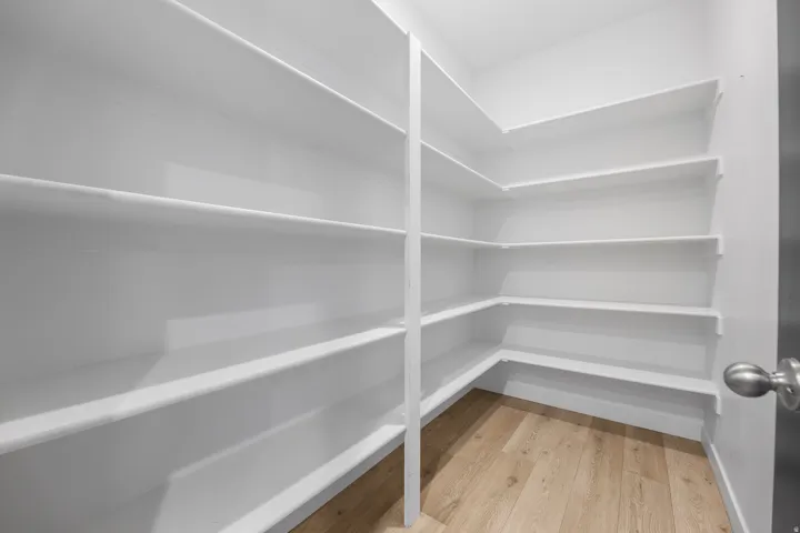 Spacious pantry featuring extensive white shelving, wood-finish flooring, and a satin nickel door knob