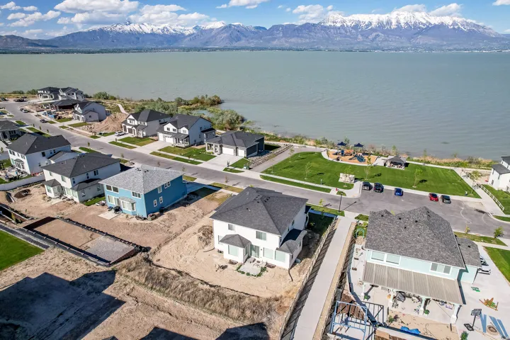 Aerial perspective showcasing a residential community situated along a expansive body of water, featuring snow-capped mountains in the background