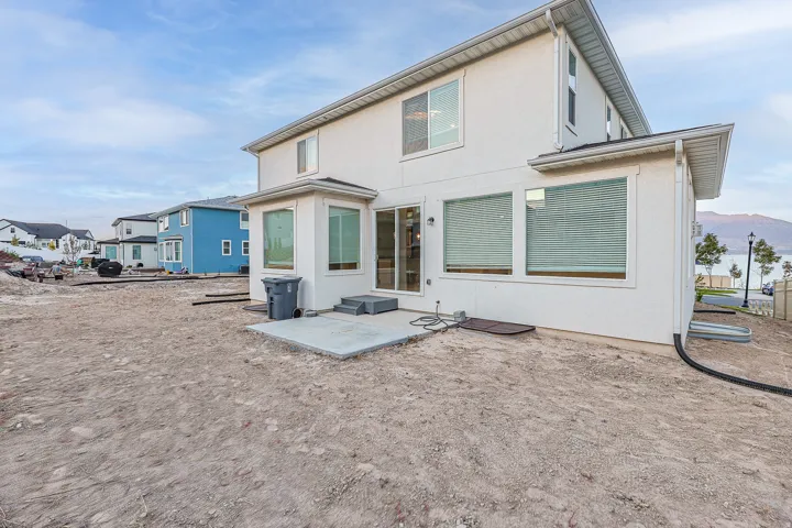 Rear exterior featuring light-colored stucco siding, multiple windows, and a concrete patio