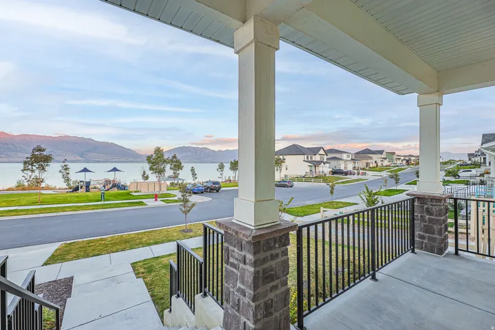Front porch featuring a concrete surface, white columns with stone bases, and black metal railings