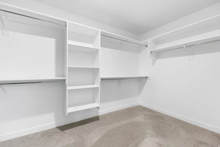 Walk-in closet featuring built-in shelving, multiple hanging rods, and neutral-toned carpeting