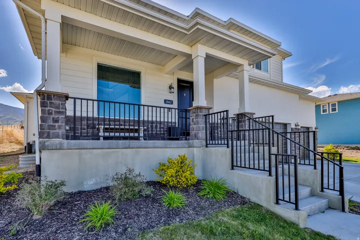 Contemporary home exterior featuring a covered front porch with stone-clad columns and black metal railings