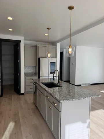Kitchen featuring a center island with a black sink and gold-tone faucet, light gray cabinetry, stainless steel appliances, and wood-finish flooring