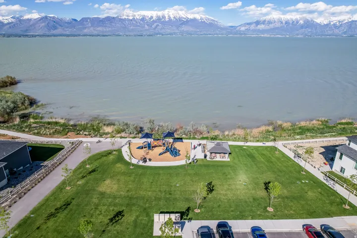 Expansive green space featuring a playground, shaded pavilion, and direct access to a paved walking path along the waterfront