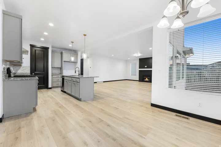 Open-concept living area featuring wood-finish flooring, a kitchen island with sink, gray cabinetry, and a fireplace with a dark surround