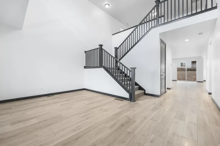 Spacious entryway featuring light wood-finish flooring, a two-story ceiling, a staircase with dark balusters and handrails, and recessed lighting