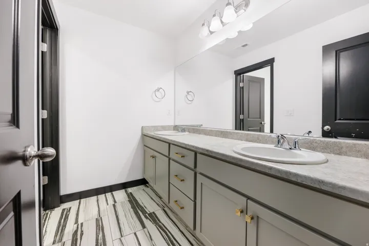 Bathroom vanity featuring dual sinks with chrome fixtures, a full-width mirror, and multi-bulb lighting
