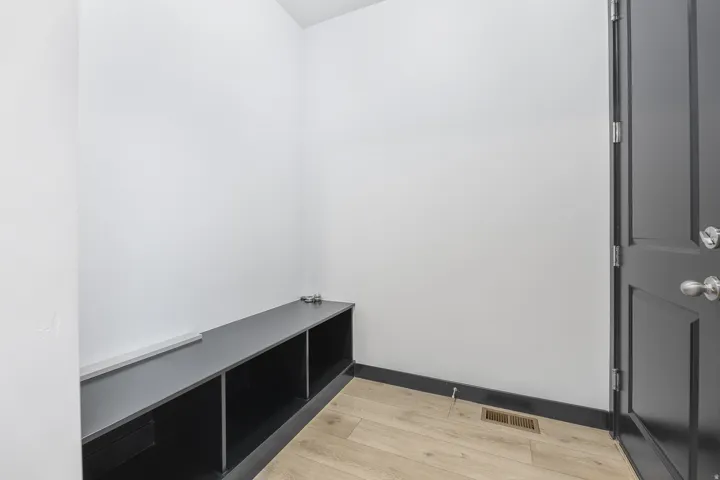 Built-in storage bench with three cubby compartments, light wood-finish flooring, dark baseboards, and a dark paneled door with brushed nickel hardware
