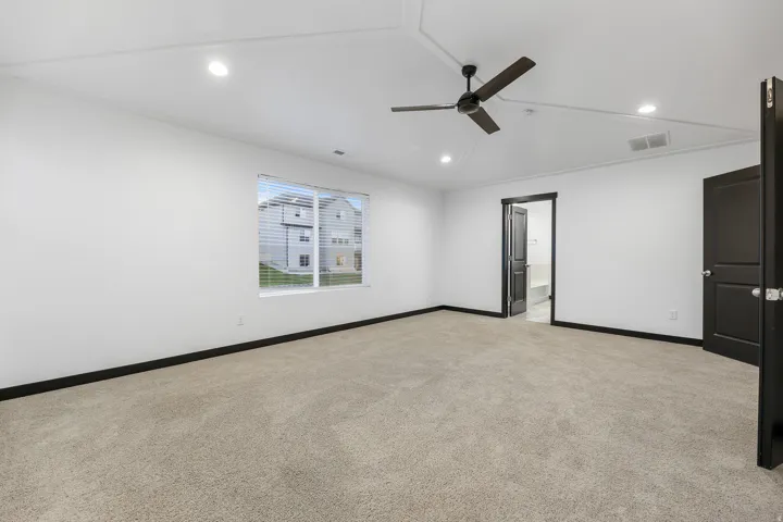 Spacious carpeted room featuring a ceiling fan, recessed lighting, white walls, dark trim, and a window with blinds