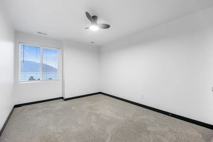 Spacious room featuring neutral carpeting, a large window with horizontal blinds, and a modern ceiling fan with integrated lighting