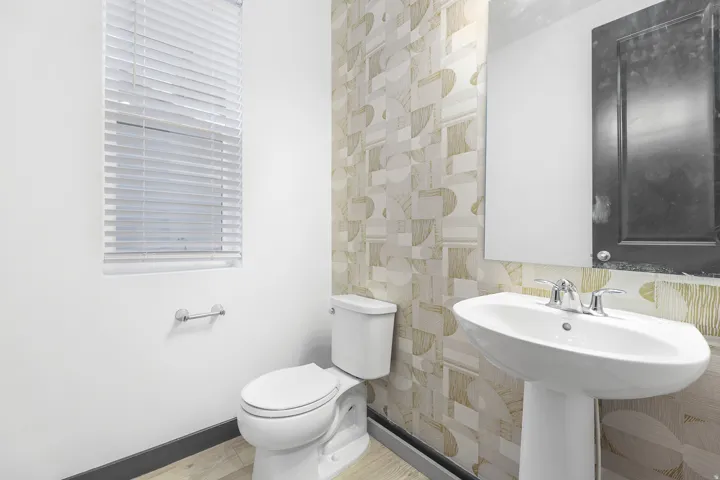 Pedestal sink with chrome faucet, complemented by a geometric-patterned accent wall