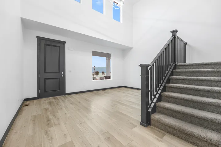 Two-story entryway with light wood-finish flooring and a dark wood staircase featuring carpeted treads