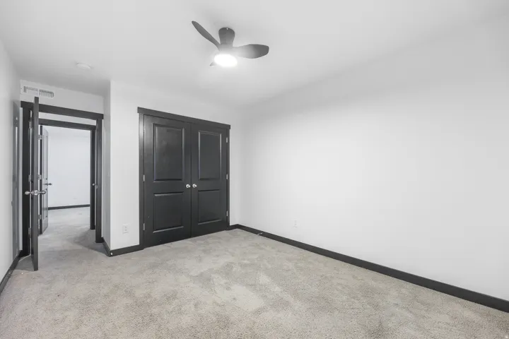 Light gray carpeted room featuring a ceiling fan with integrated lighting, dark bi-fold closet doors, and contrasting dark trim